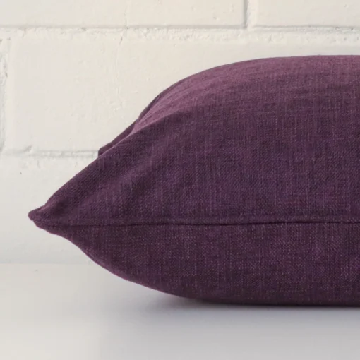 Square plum cushion laid flat. This view shows the linen fabric from side on.