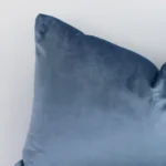 A velvet rectangle cushion’s corner has been enlarged in this shot. The detail of the solid colour design and stone blue colour are visible.