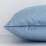 A rectangle stone blue cushion cover laying flat. This viewpoint highlights the solid colour style and velvet fabric from a side position.