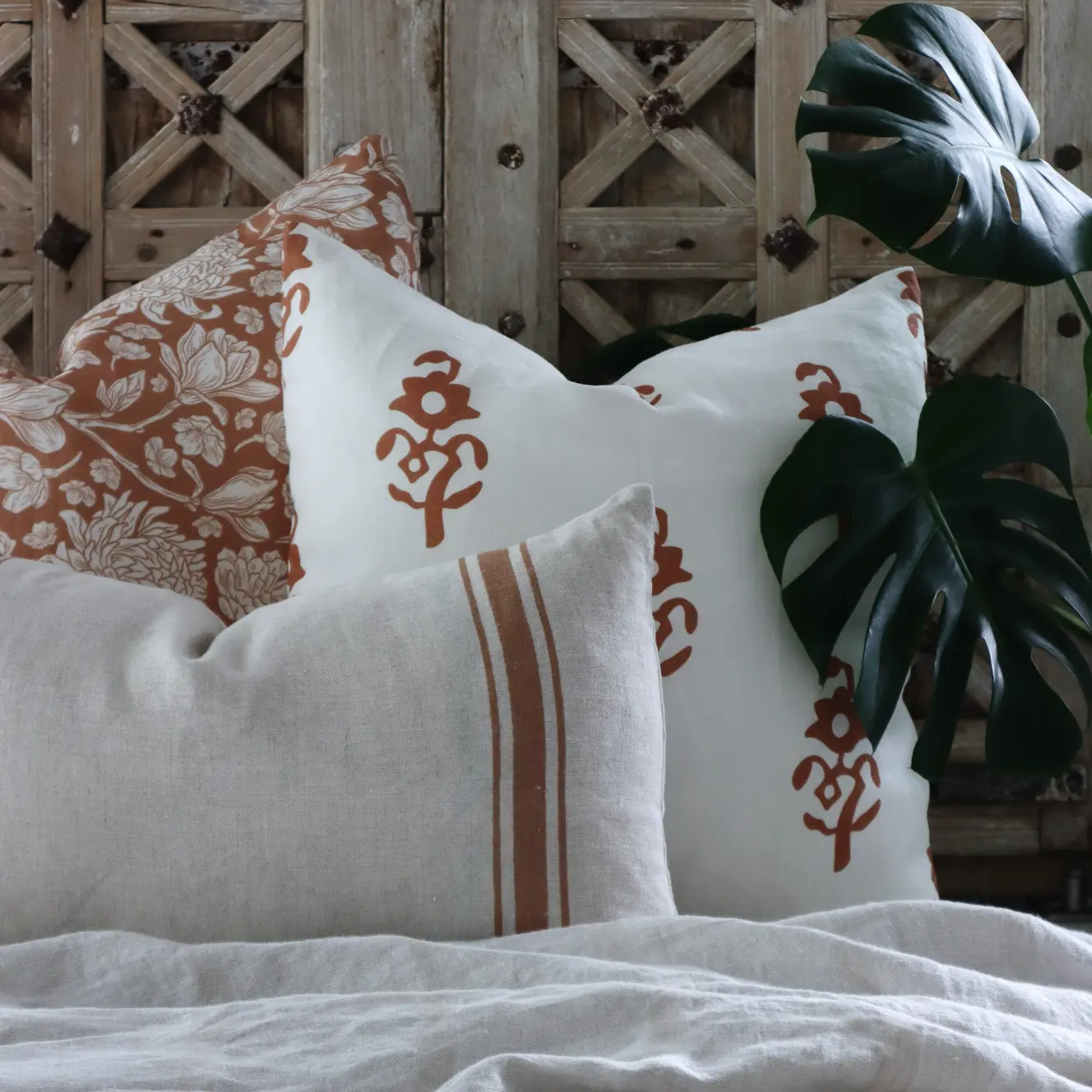 An ornate wooden door has some coordinated cushions arranged in front of it along with a throw.