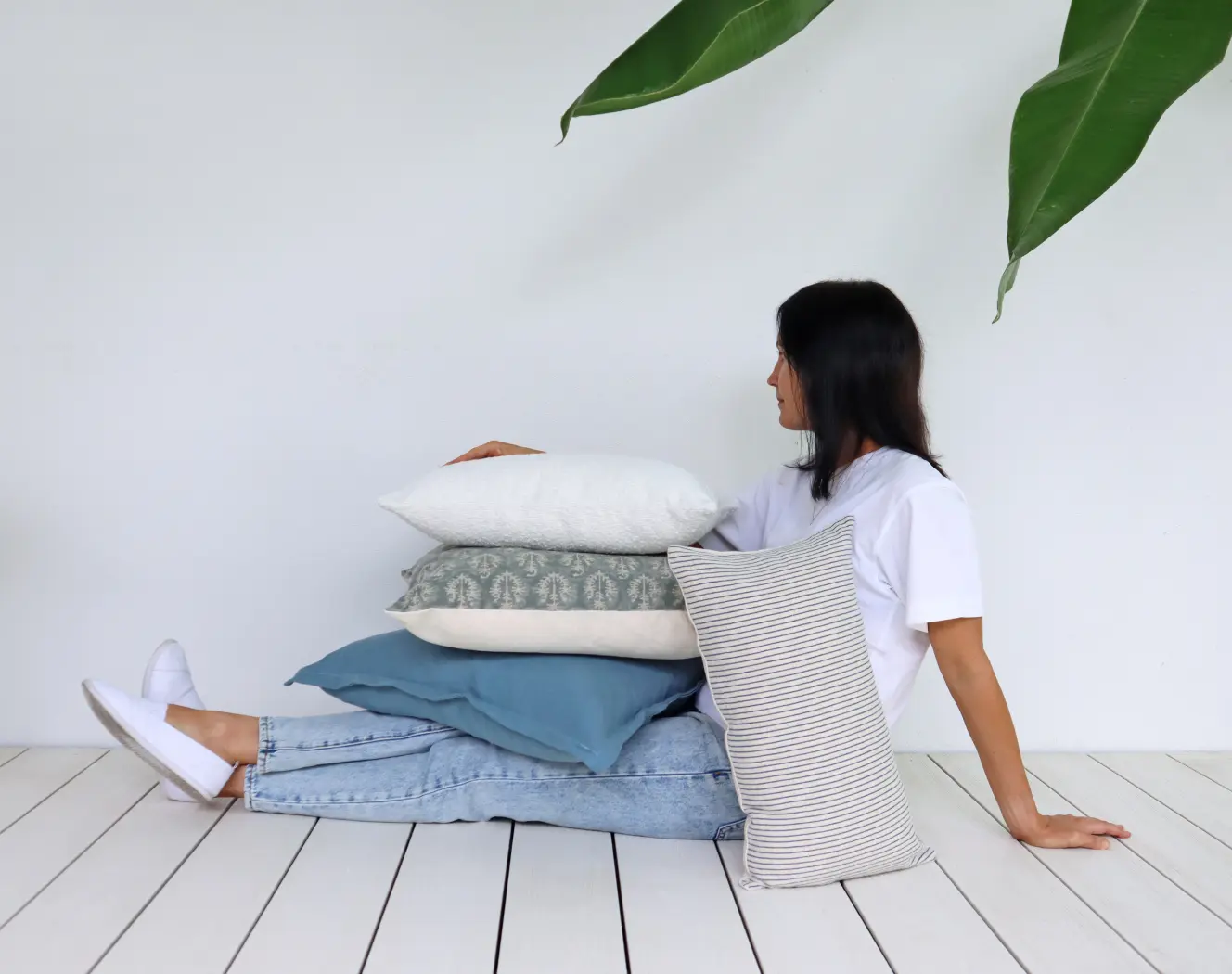 A woman is sitting with legs out holding cushion covers in various designs and sizes.