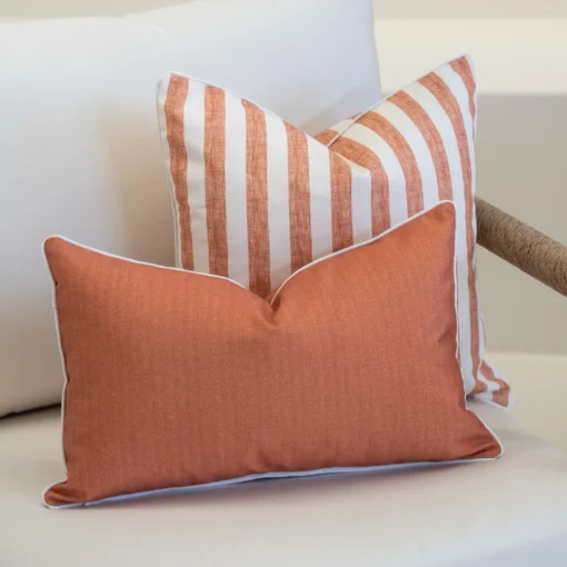 A white sofa with a set of 2 pacific rust outdoor cushions sitting on it.